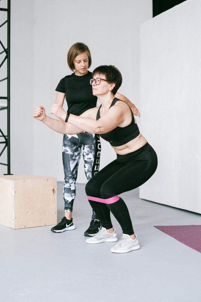 Assessments & Myofascial Trigger Therapy Two women exercising indoors with resistance bands, focusing on balance and fitness.